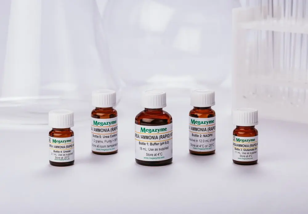 Fem bruna Megazyme-reagensflaskor med vita lock, märkta Urea/Ammonia Rapid Kit, på en laboratoriebänk.